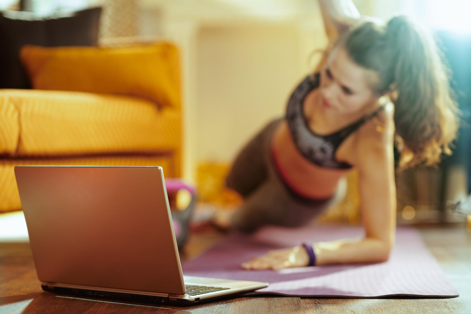 Closeup on laptop and woman in background doing cardio exercises